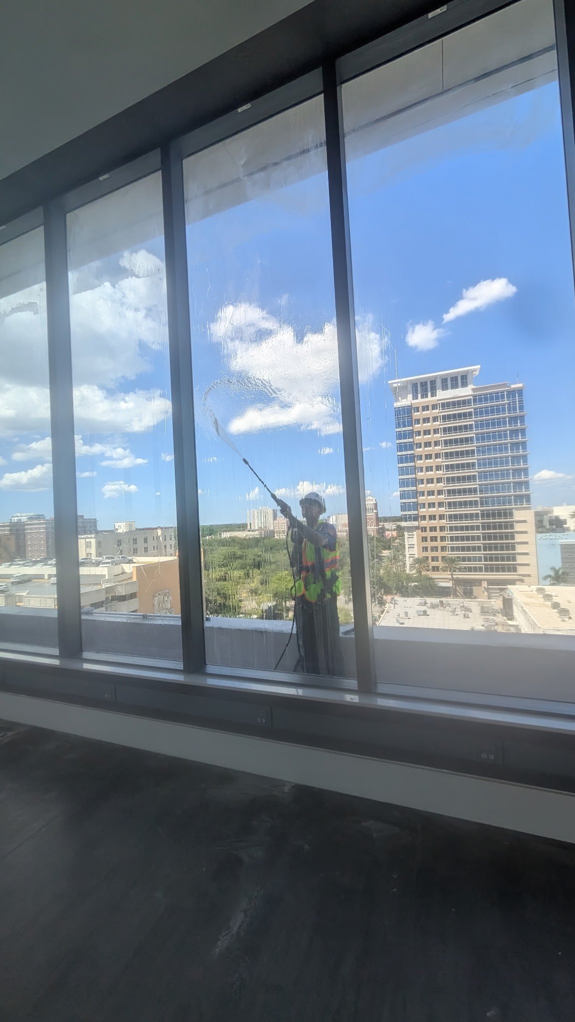 High-rise glass windows being rinsed from a lift with squeegee and pressure spray, city skyline beyond