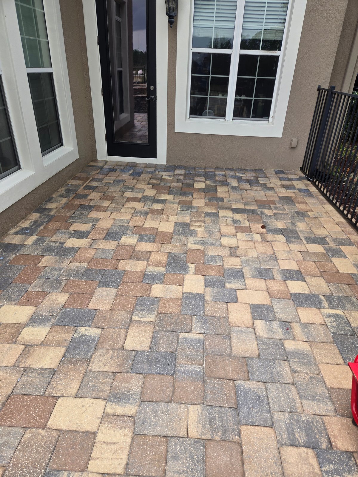 Patio with geometric patterned pavers in tan and gray tones, flanked by white-framed doors and windows on a beige house exterior
