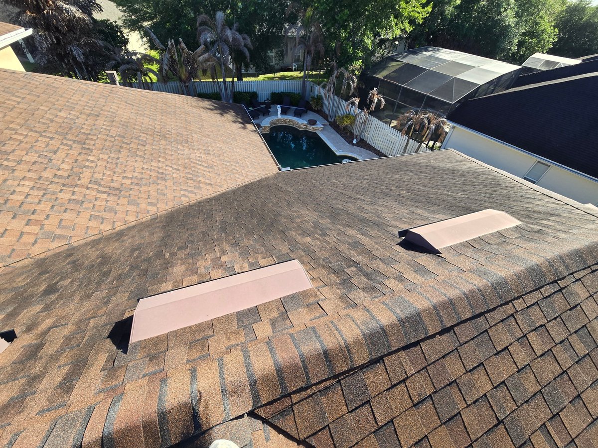 Residential roofing with two light-colored rectangular patches on asphalt shingles, pool and green trees visible in background