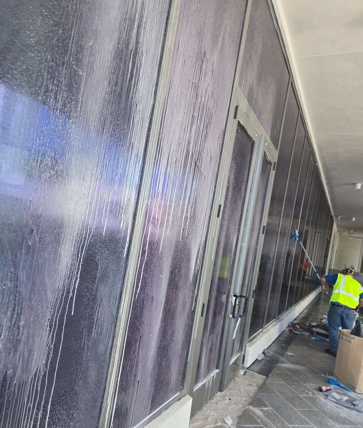 Worker in yellow safety vest spraying water on corrugated metal wall to clean it