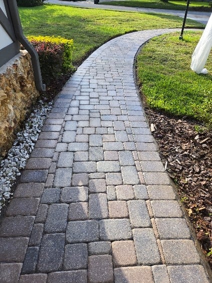 Curved paver walkway with herringbone pattern bordered by green lawn and mulch landscaping
