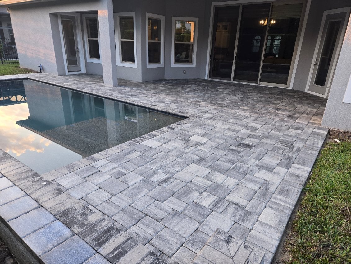 Modern backyard with rectangular pool and gray paver patio adjacent to white house with large glass doors