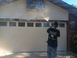 Person in black shirt standing in front of a white garage door with brick pillar on a sunny day