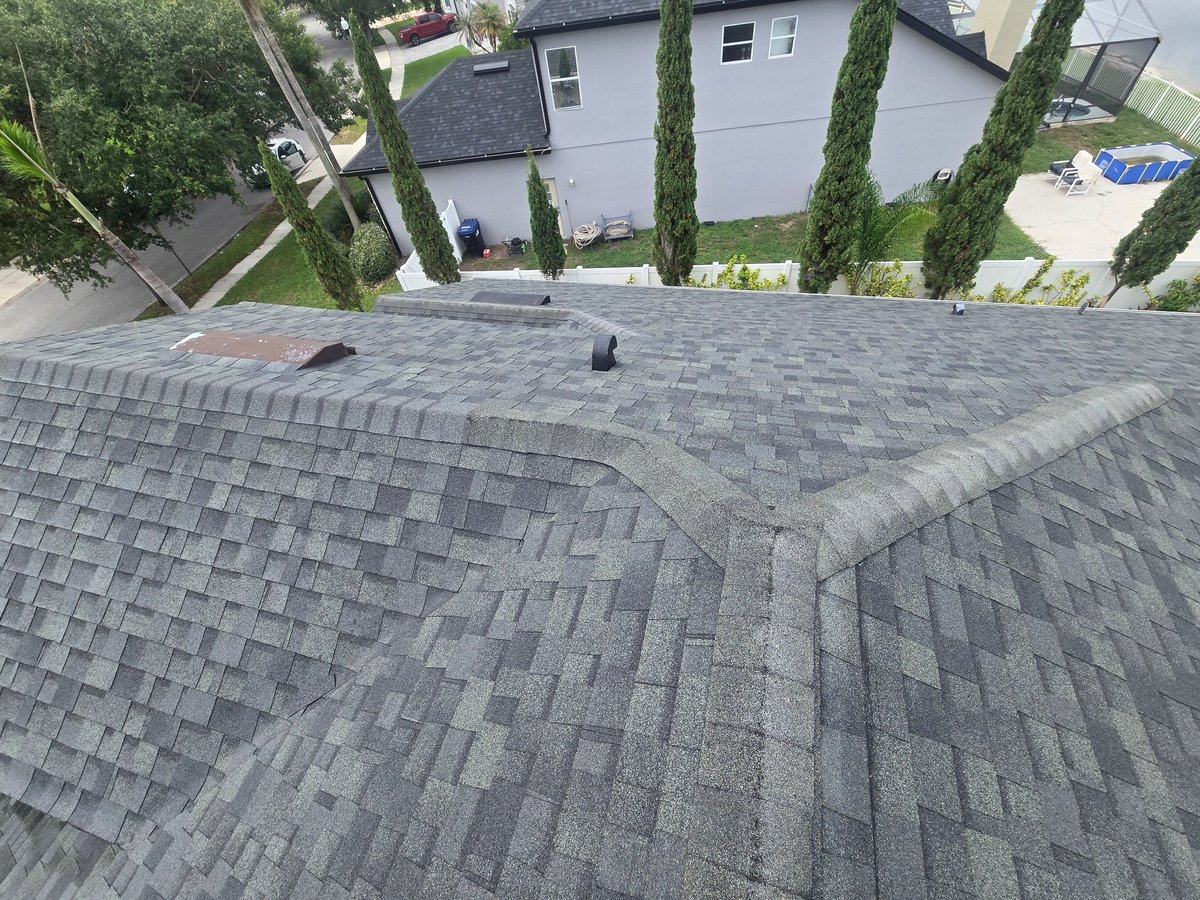 Aerial view of gray asphalt shingle roof with valley, residential home and landscaped yard visible below