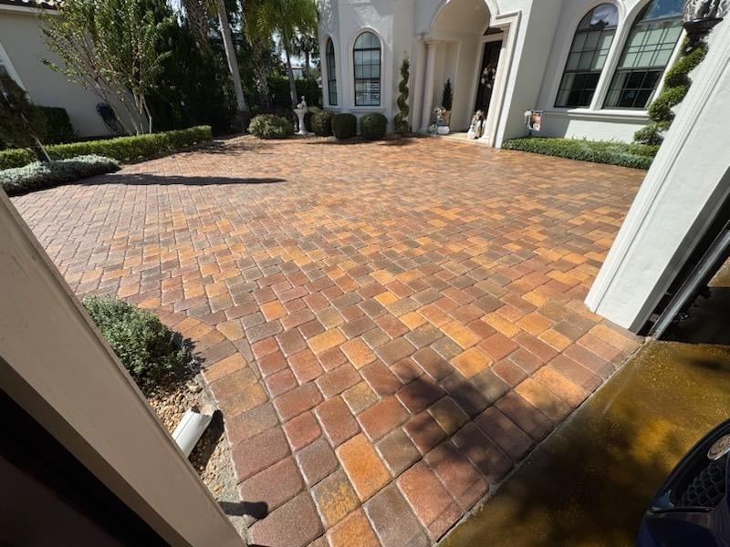 Brick paved driveway in front of a white Mediterranean-style home with landscaping
