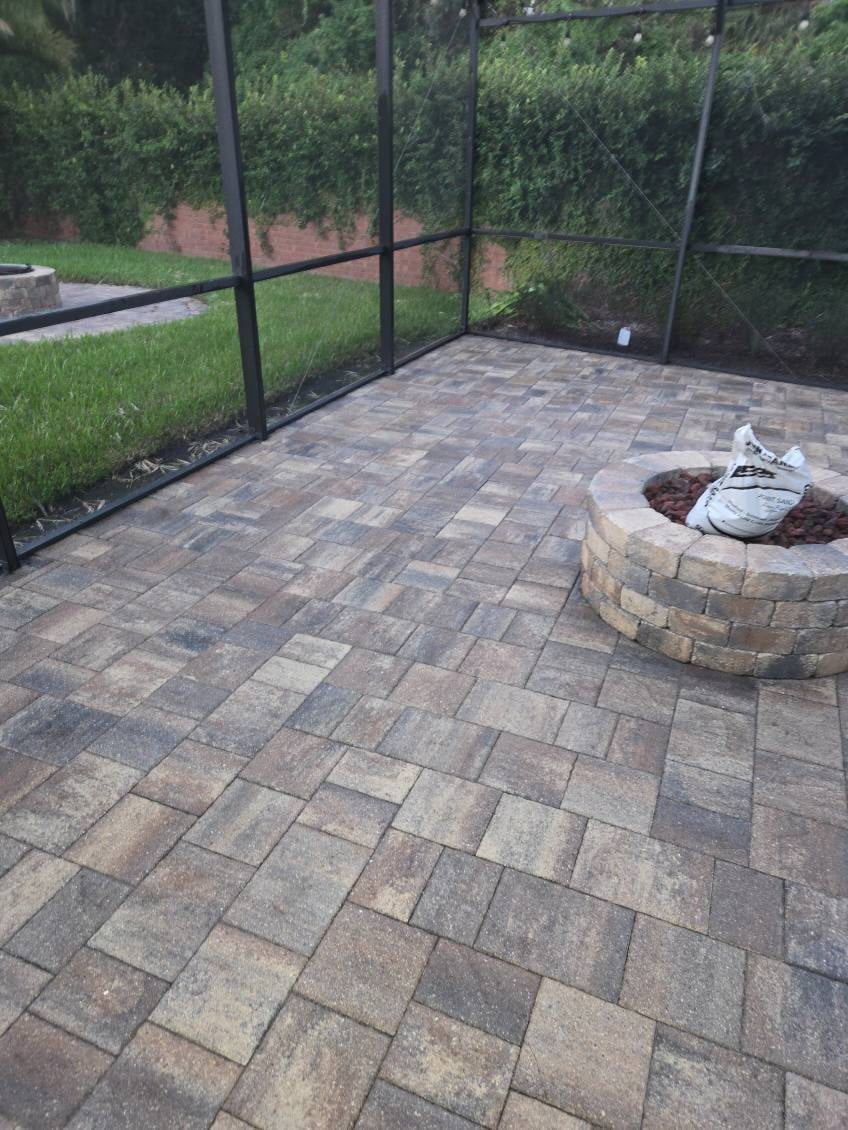 Paved patio with fire pit ring inside a screened enclosure surrounded by green lawn and shrubs