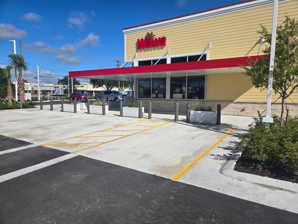 Exterior of a Wawa convenience store with red awning, concrete patio, and parking area on a sunny day
