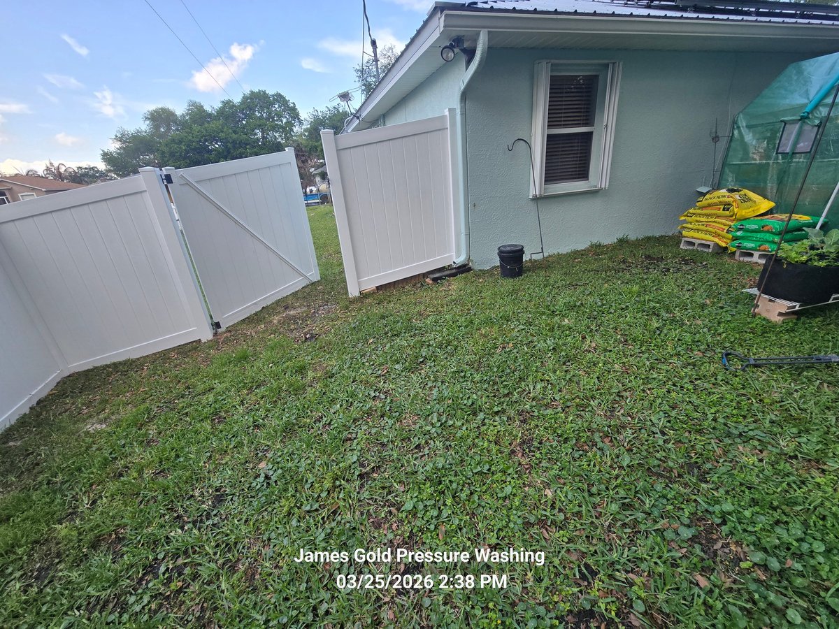 Small residential building with a clean white metal fence and green lawn in the backyard