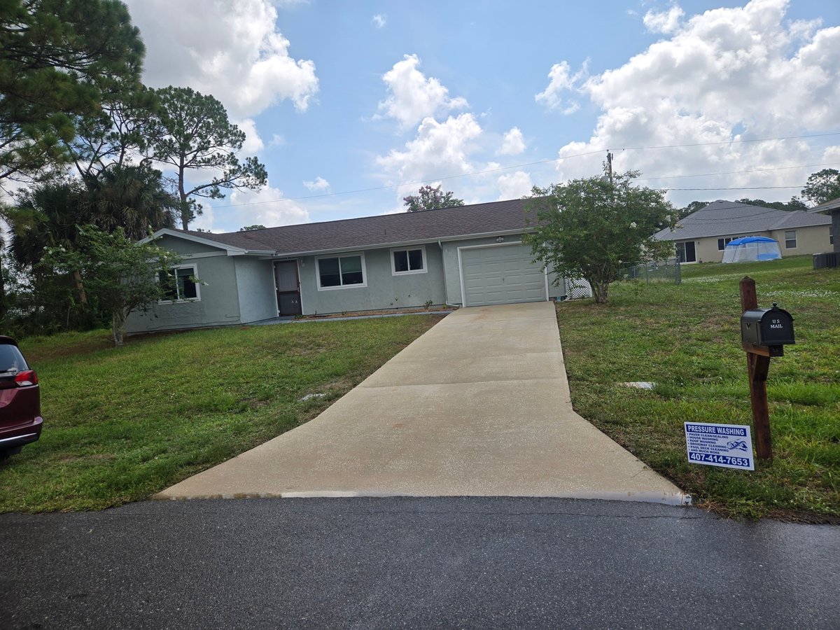 Single-story residential house with attached garage and clean concrete driveway in a suburban neighborhood