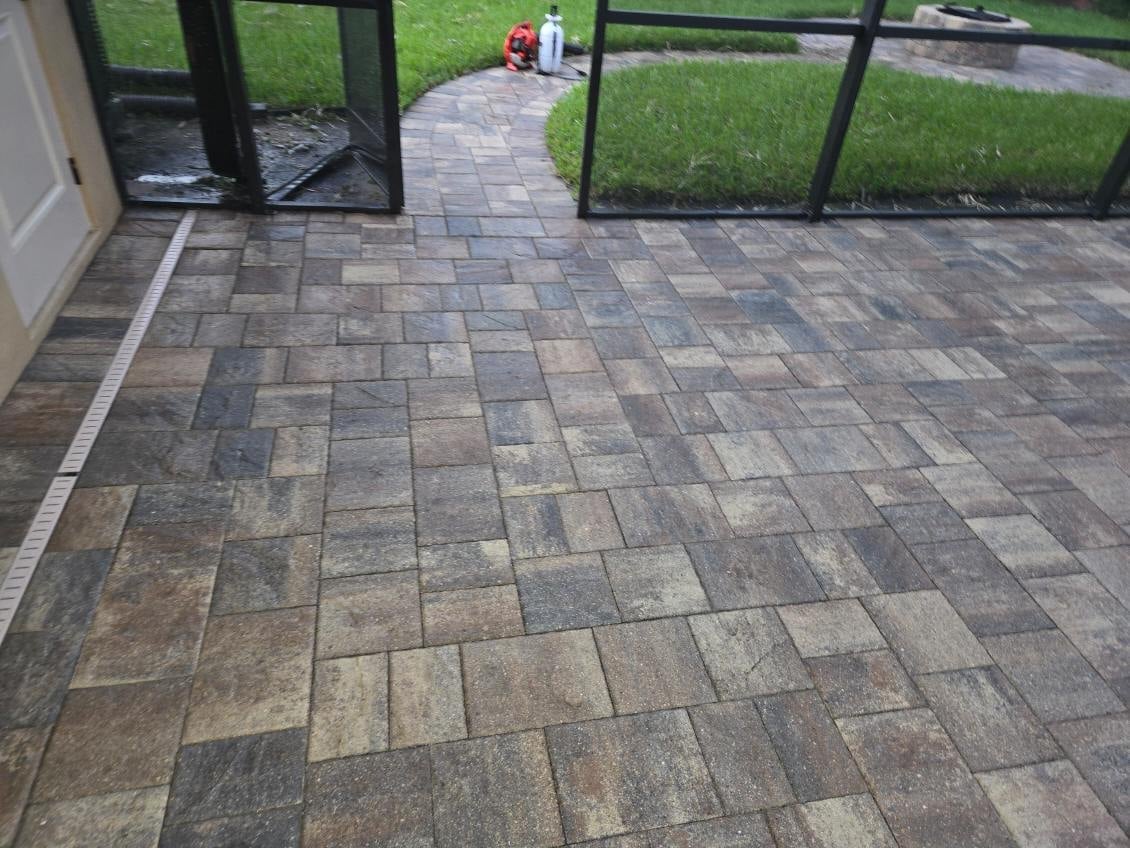 Herringbone patterned paver patio with black framed doors opening to green lawn and red plastic chair visible in background