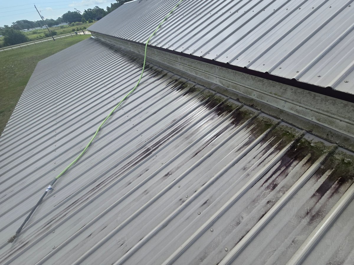 Aerial view of metal corrugated roof with moss and algae growth, showing agricultural fields in the background