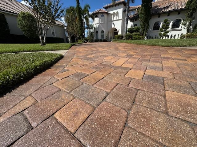 Paved driveway with geometric brick pattern leading to Mediterranean-style villa surrounded by manicured landscaping