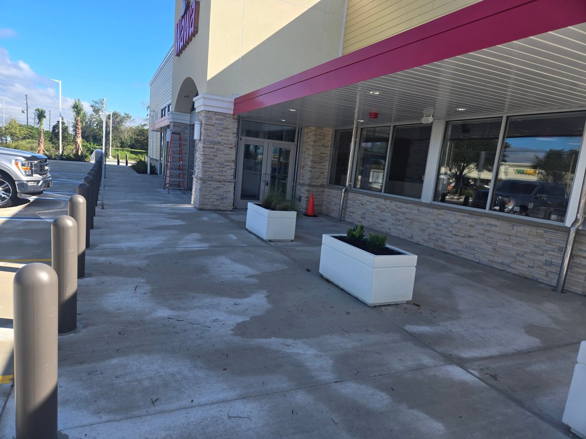Storefront exterior with concrete walkway, white planters, glass entrance doors, and burgundy awning in bright daylight