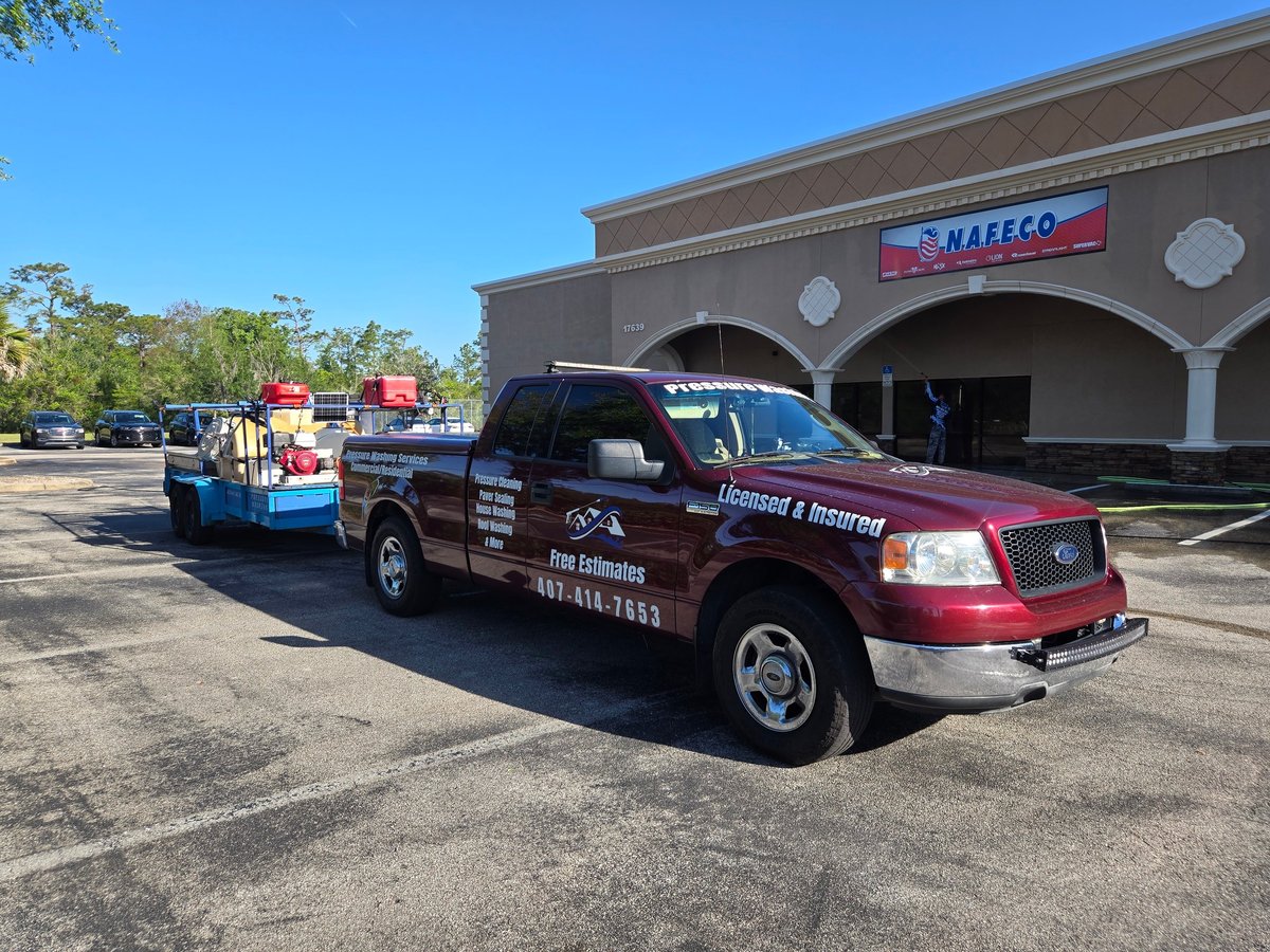 Red Ford pickup with James Gold Pressure Washing signage and trailer parked in front of a commercial building during a job