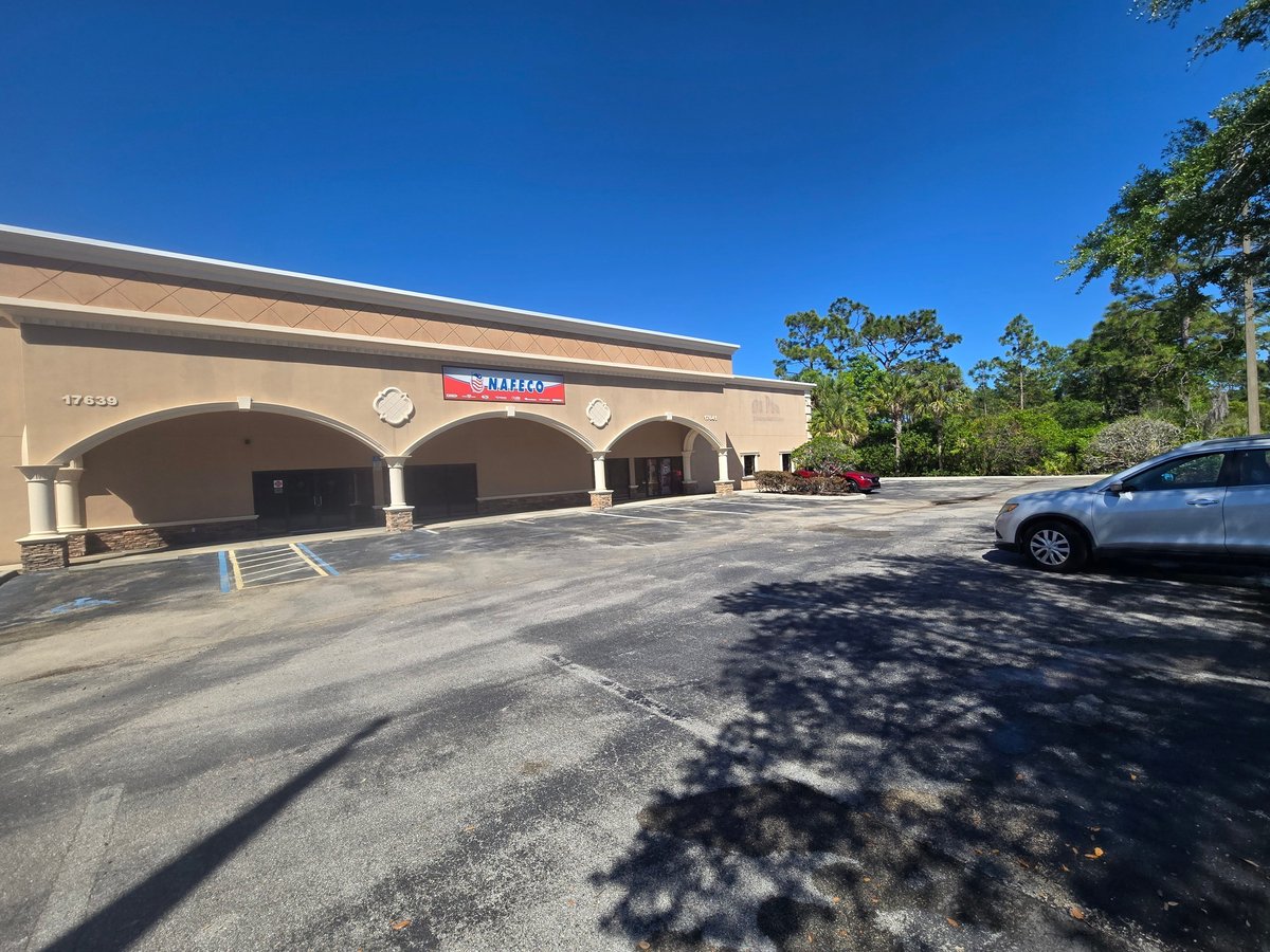 Beige commercial building with arched entrance and clean parking lot with vehicles under a clear blue sky