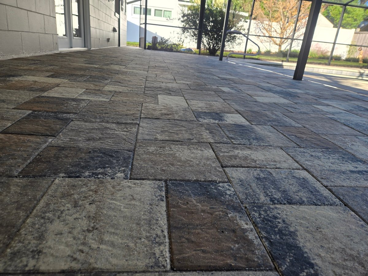 Covered lanai paver floor with weathered, stained stone tiles under a screen enclosure before cleaning