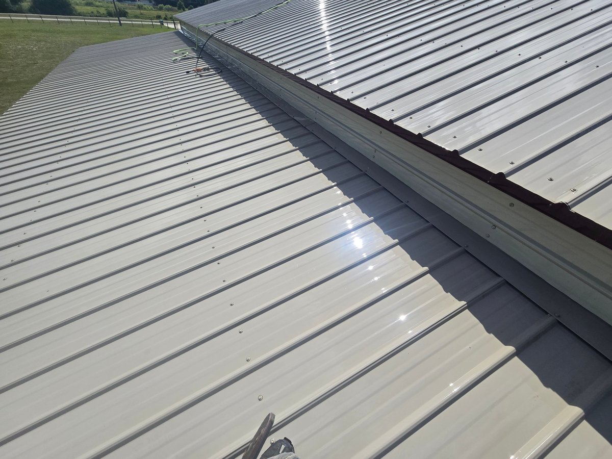 Close-up view of a metal corrugated roof with horizontal ridges and an expansion joint, with green landscape visible in background
