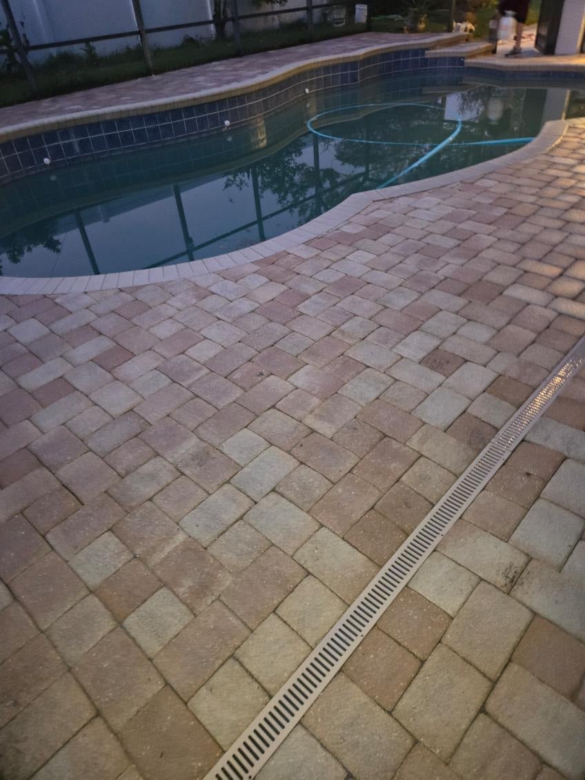 Swimming pool with tiled edge and surrounding paver deck at dusk, with landscape lighting in background