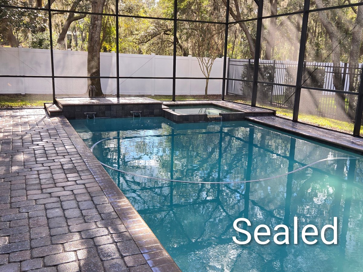Screened-in swimming pool with clear turquoise water and sealed brick deck surrounded by trees