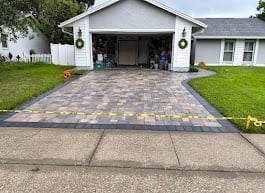 Brick paver driveway leading to two-car garage of white suburban home with manicured lawn