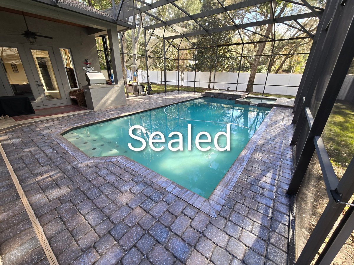 Sealed outdoor swimming pool with turquoise water, brick patio, and screened enclosure attached to modern home