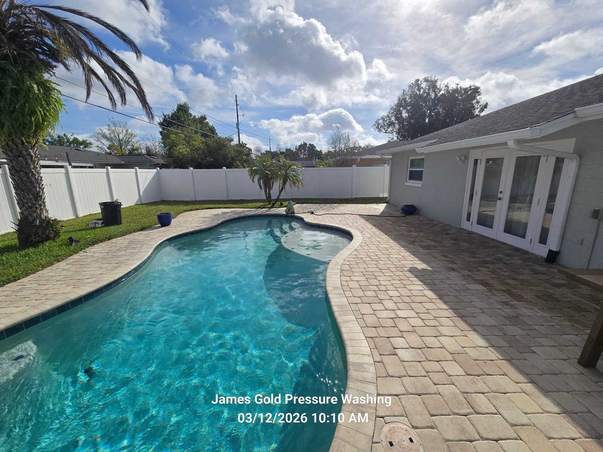 Backyard pool with clear turquoise water, patio, white fence, and white pool house under sunny skies with clouds
