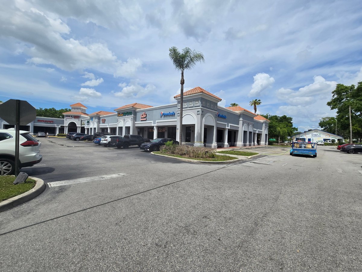 White commercial building with columns and palm tree at the center, cleaned parking lot in front on a sunny day