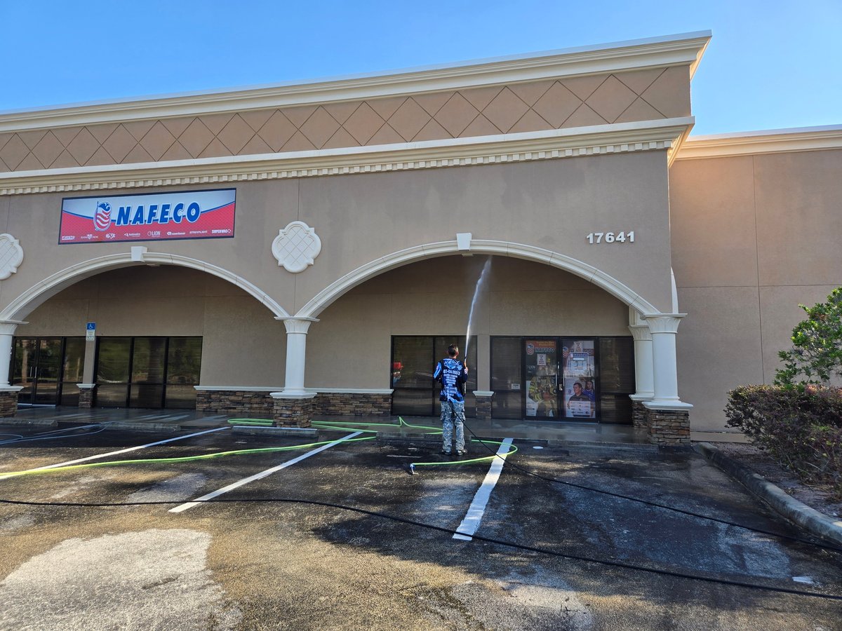 Crew pressure washing the exterior and parking area of a Nafeco storefront with beige walls and white arches