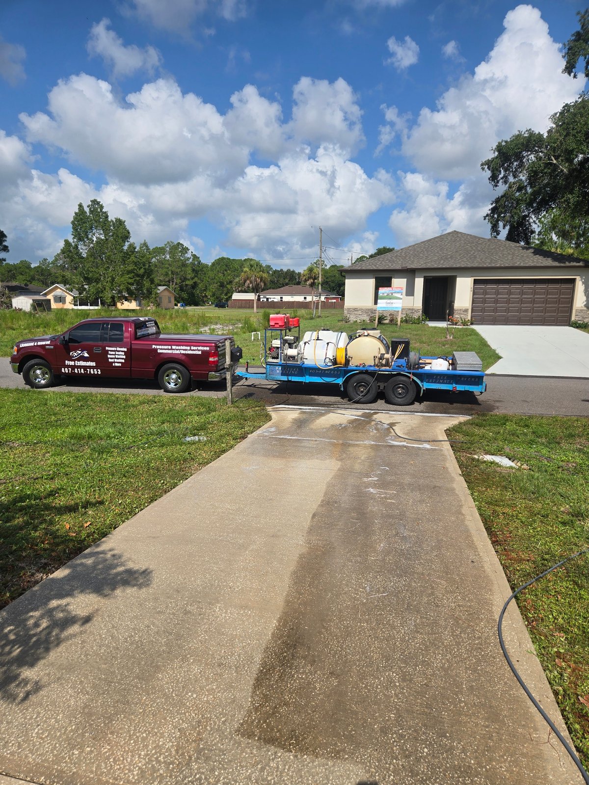 Maroon pickup truck with blue equipment trailer parked in residential driveway on sunny day
