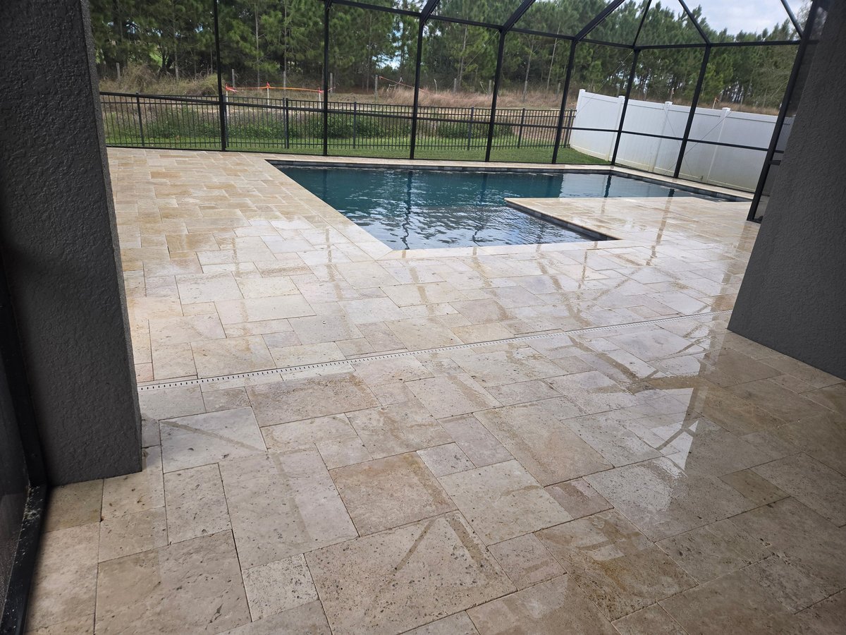 Rectangular swimming pool with black safety fence on travertine patio surrounded by trees and water view