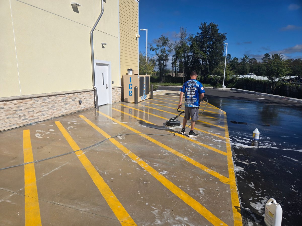 Man standing on wet commercial rooftop with yellow safety lines and equipment, clear blue sky visible.