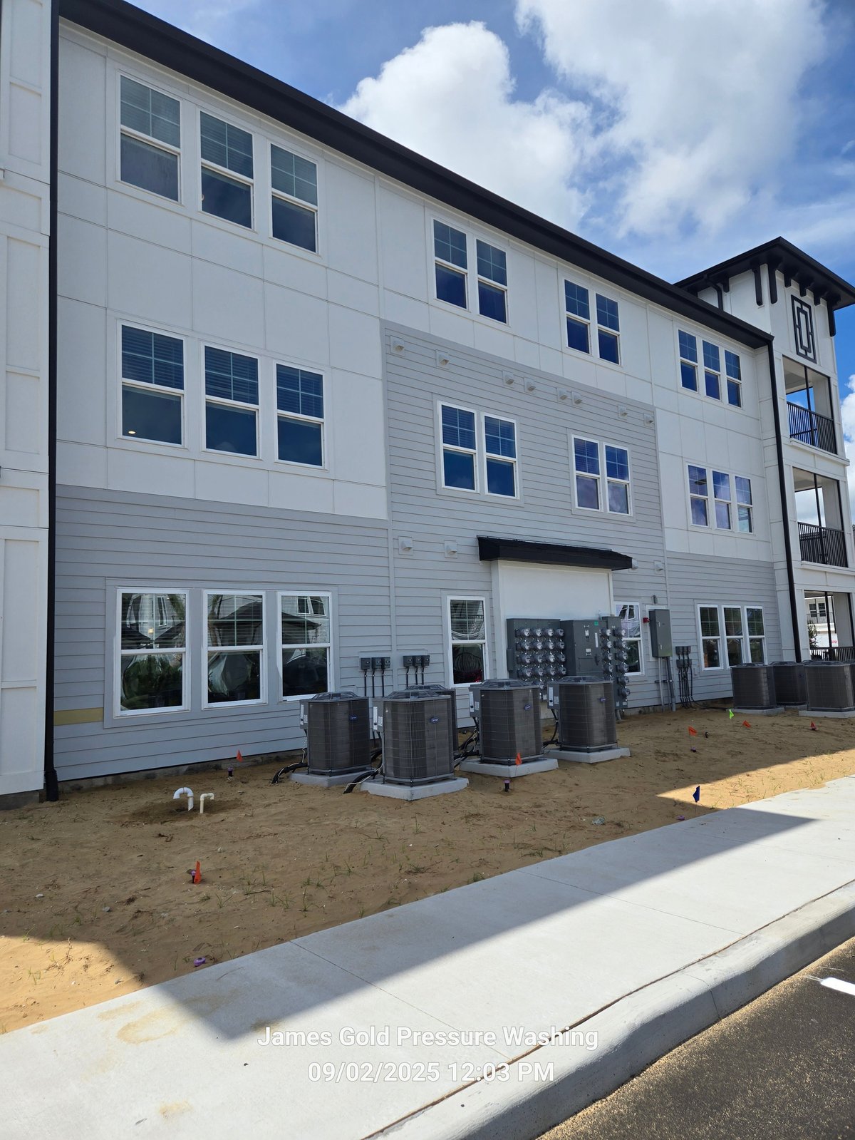 Modern white multi-story residential building with HVAC units on sandy ground and blue sky background