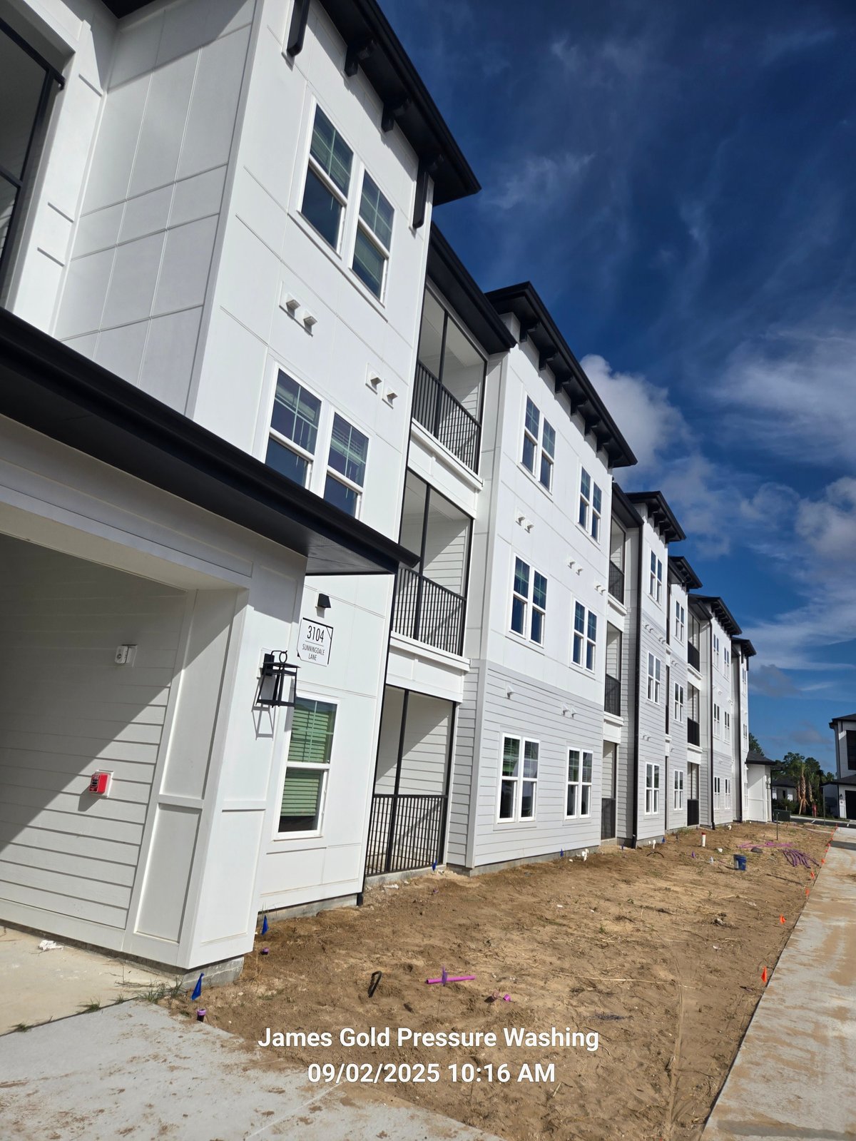 New white townhouses under construction with dark roofs against a blue sky, bare ground yard visible