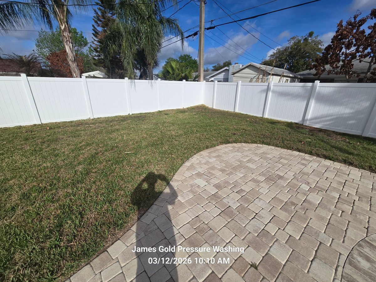 Backyard with white vinyl fence, green grass, paver patio, and trees under blue sky